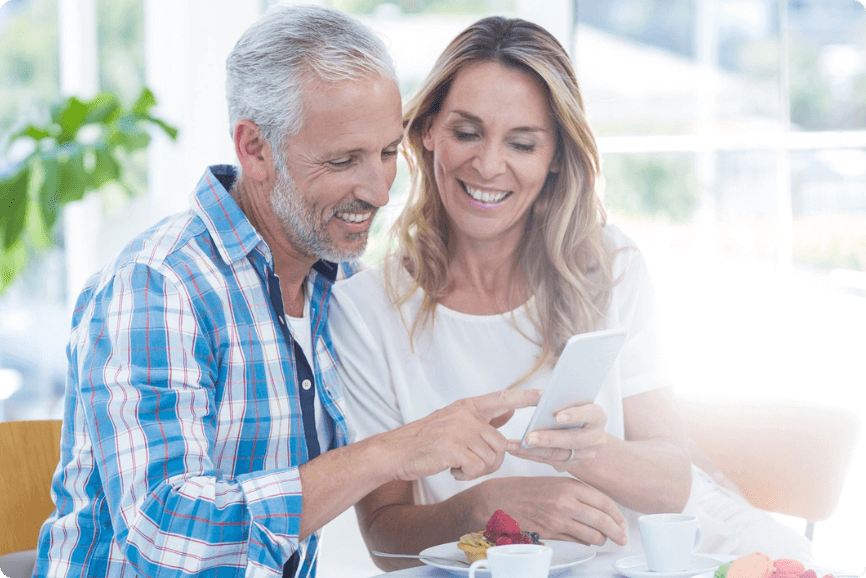 Older couple sitting on a dining room table and looking at a cell phone