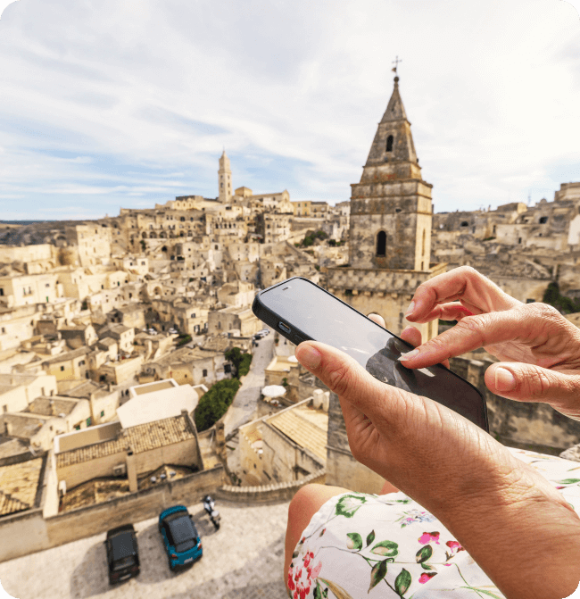 Woman in flower print dress scrolling with phone in hand while overlooking historic city.